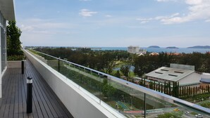 Un balcon offrant une vue sur une zone côtière, comprenant une route, de la végétation et des bâtiments.