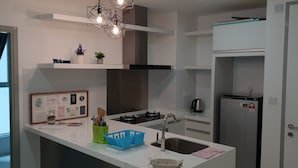 Une cuisine moderne avec des meubles blancs, un réfrigérateur en acier inoxydable, une cuisinière à gaz et un four encastré. On y trouve également des plantes décoratives et un tableau encadré posé sur le plan de travail.