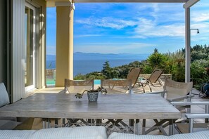 Relax in a serene outdoor seating area with a stunning sea view, featuring a table, potted plant, and comfortable chairs.