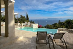 Relax by the pool with a view of the sea and distant mountains.