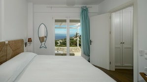 A bedroom with a bed, a wall-mounted lamp, a fish-shaped mirror, and a view of the sea through a glass door. - Apeiron II Villa - Two Bedroom Villa, Sleeps 4 (Paxi)