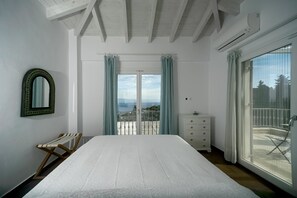 Relax in this serene bedroom with a large bed, a balcony offering a view of the outdoors, and a dresser for your belongings.