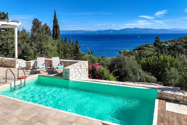 Relax by the serene pool surrounded by lush greenery and breathtaking views of the sea and distant mountains.