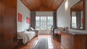Une chambre avec un plafond en bois, un lit, une commode, une chaise, un bureau et une grande fenêtre avec des rideaux.