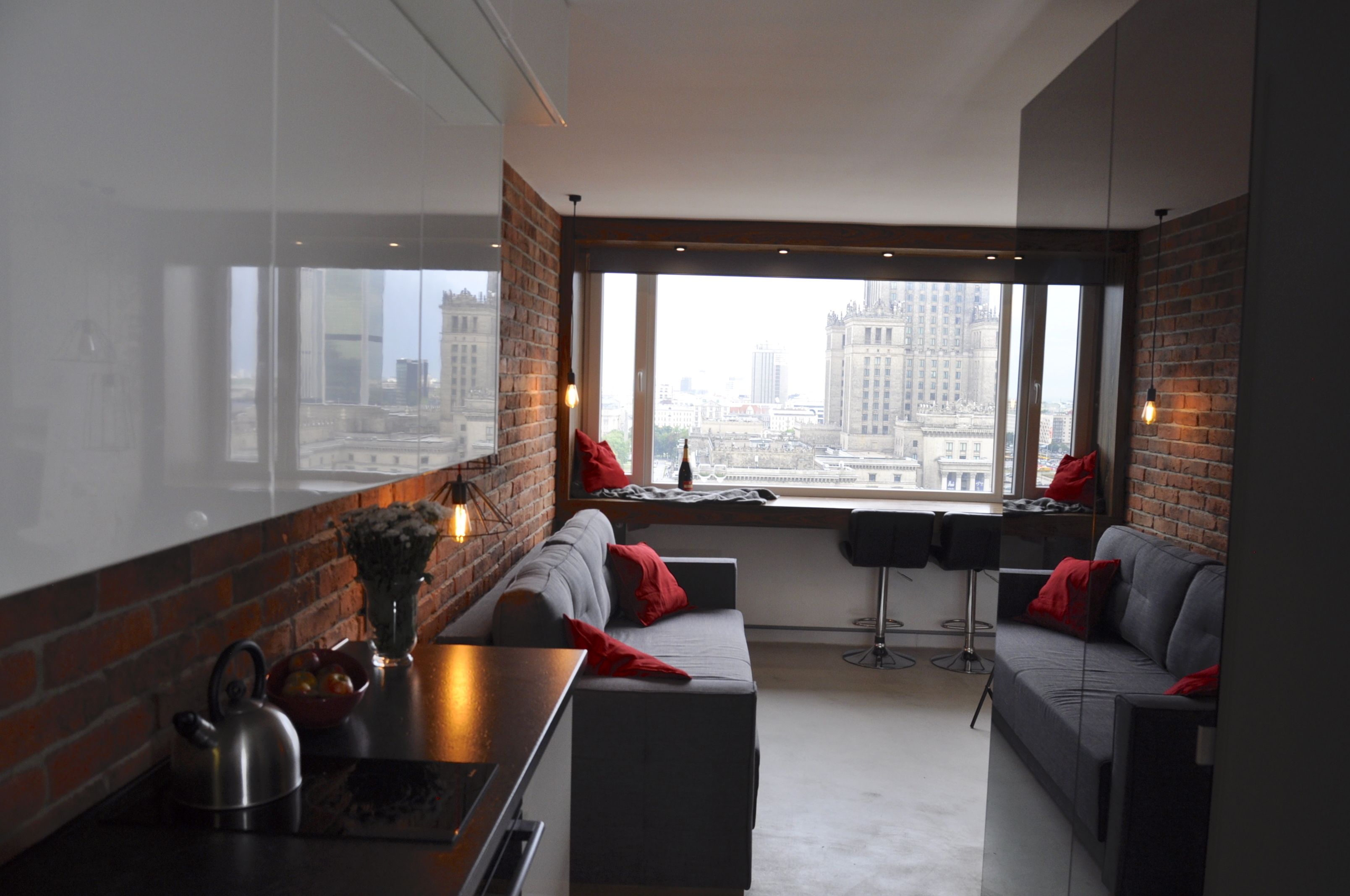 Ein modernes Wohnzimmer mit Blick auf die Stadt, eine Küchenzeile mit Wasserkocher und ein Esstisch mit Stühlen.