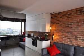 A modern kitchen with a glass partition, a grey sofa with a red pillow, and a brick wall. - Panda Apartments Bagno- Centrum (Warsaw)