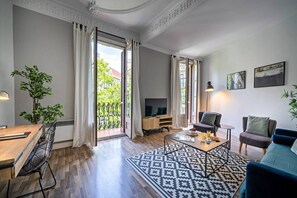 A modern living room with a wooden coffee table, a sofa, a TV, and a balcony with a view of buildings.