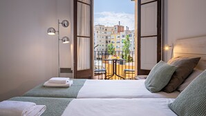 A hotel room with two beds, a balcony with a table and chairs, and a view of buildings. - Barcelona Balconies 1 - Habitat Apartments (Barcelona)