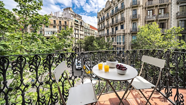 A balcony with a table set for breakfast, including a bowl of fruit and two glasses of orange juice. - Barcelona Balconies 1 - Habitat Apartments (Barcelona)