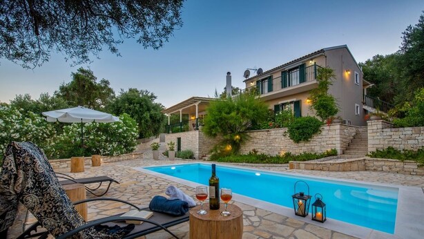 Zona de piscina con patio de piedra, una silla de descanso, una mesa con botella y vaso, y una casa al fondo.