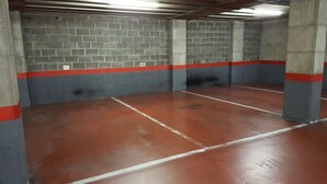 Un parking avec des piliers en béton, des murs rouges et gris, et des places de stationnement numérotées.