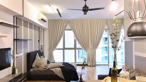 Quarto de hotel moderno com cama, televisão, ventoinha no teto e janelas amplas com cortinas.