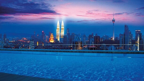 Horizonte urbano ao entardecer com edifícios imponentes, incluindo as Torres Petronas, e uma piscina em primeiro plano.
