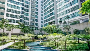 Um edifício moderno com vários andares, janelas amplas e um pátio central com um espelho d'água e vegetação.