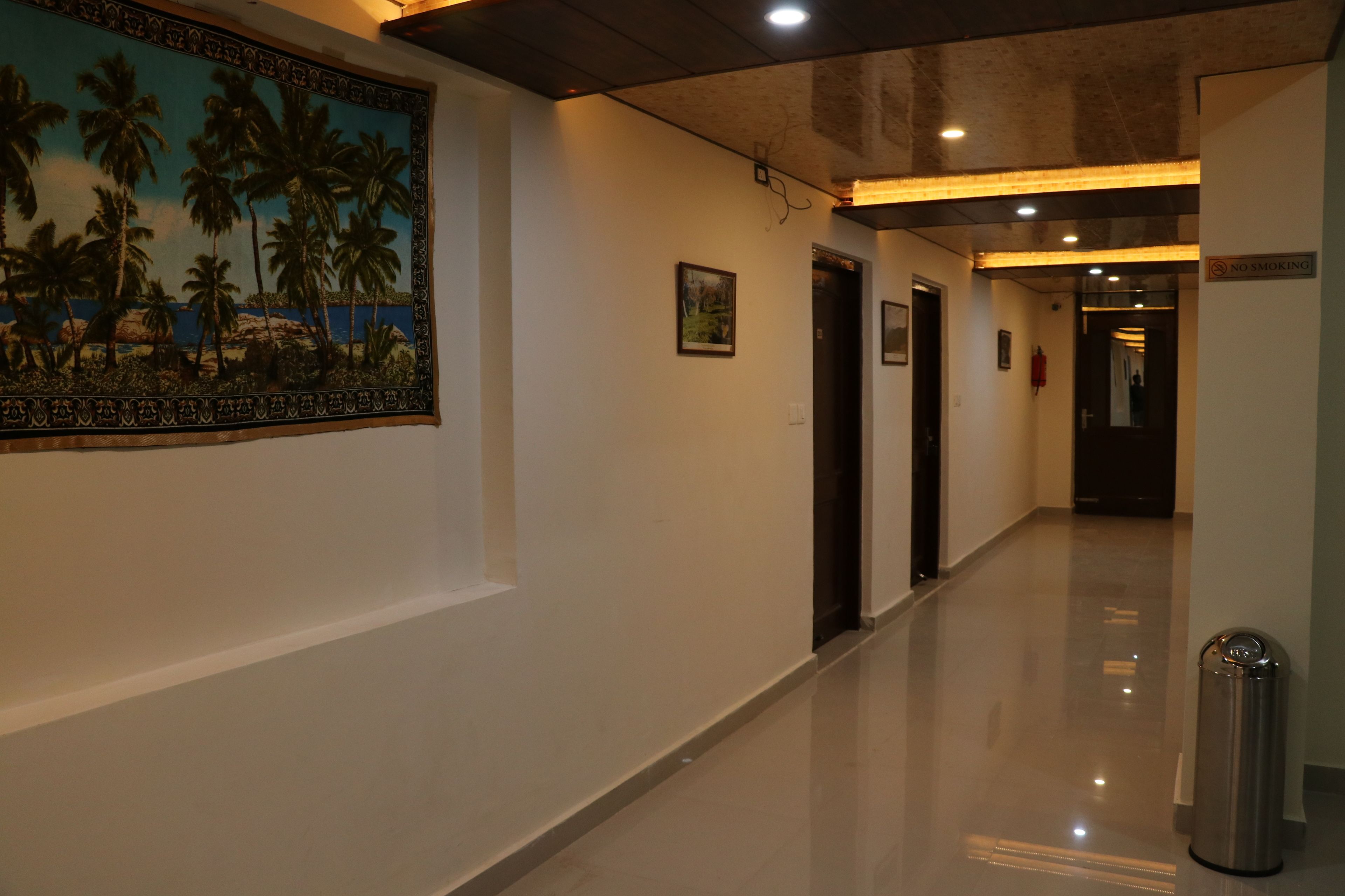 A hotel corridor with a polished floor, a tropical mural on the left wall, and a 'No Smoking' sign on the right.