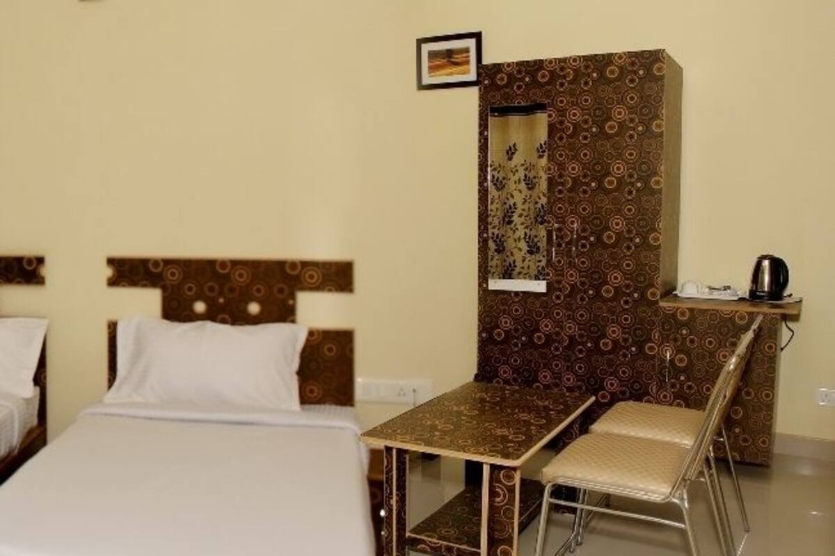 Een hotelkamer met twee enkele bedden, een klein bureau met stoel en een spiegel aan de muur.