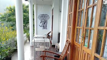 A covered outdoor area with wooden chairs and a table, white pillars, and a mural of an elephant.