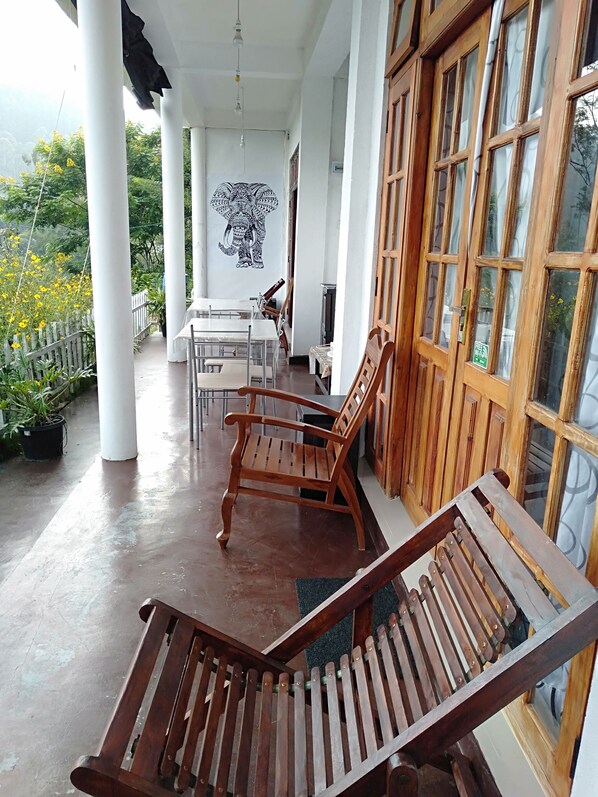 A covered outdoor area with wooden chairs and a table, white pillars, and a mural of an elephant. - Zircon Ella (Ella)