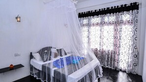 A bedroom with a bed covered by a sheer canopy, a black and white patterned curtain, and a small shelf with a decorative item. - Zircon Ella (Ella)