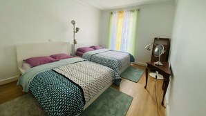 Ein Schlafzimmer mit zwei Betten, einem Schreibtisch mit Lampe und einem Fenster mit Vorhängen.