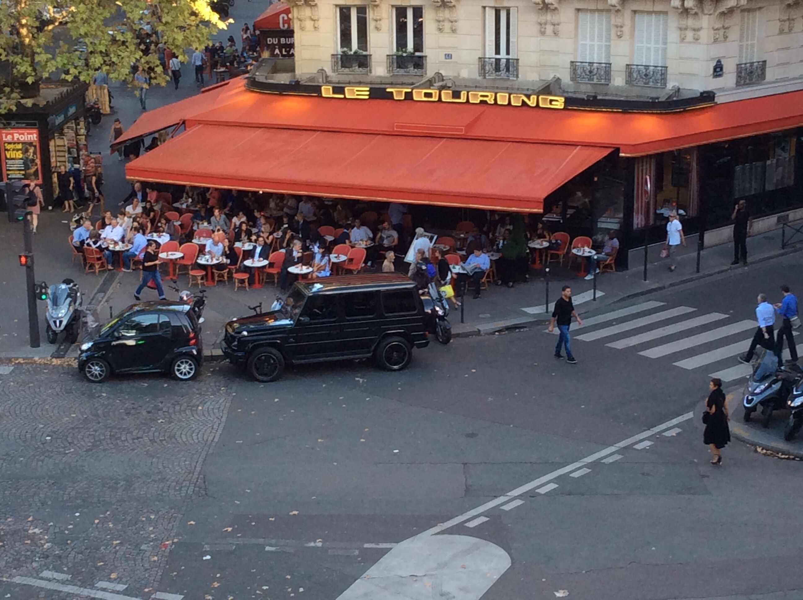 Vista de una calle con un restaurante llamado "Le Touring" que ofrece mesas al aire libre.