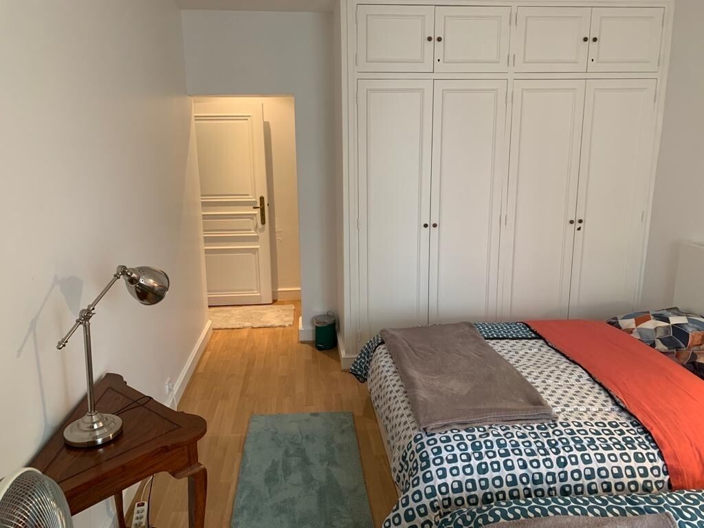 Et soveværelse med seng, skrivebord, lampe og garderobeskab.