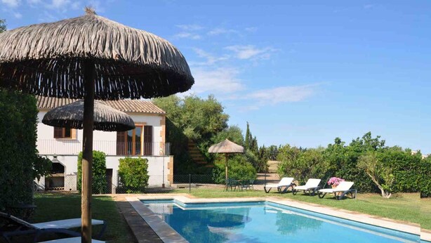 A swimming pool with lounge chairs and a thatched umbrella, surrounded by greenery and a house with a tiled roof. - Can Mostatxet, Country House in Can Picafort, Mallorca (Can Picafort)