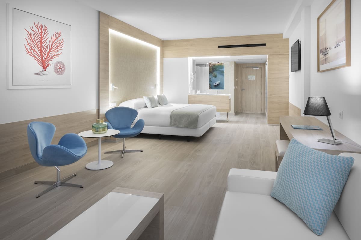 Una habitación de hotel moderna con una cama, un escritorio, una silla y un sofá. Se ve un baño al fondo.