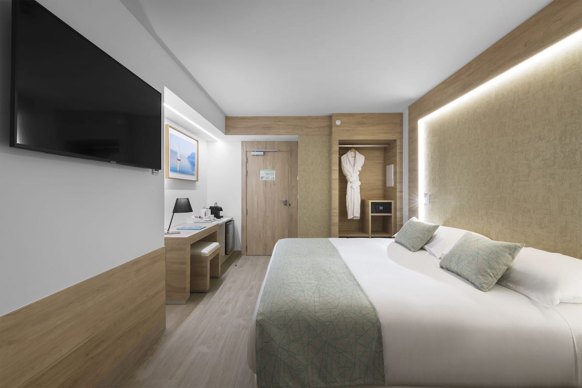 Una habitación de hotel moderna con una cama grande, un escritorio, un televisor de pantalla plana y un armario para batas.