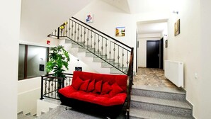 A staircase with a red sofa at the bottom, a potted plant, and a wall-mounted radiator. - Hotel Ellegance (Tbilisi)