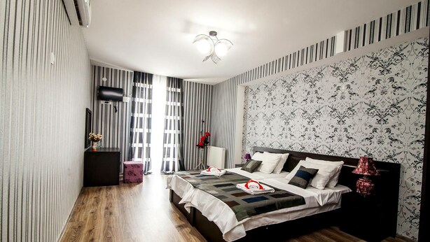 A modern bedroom with a large bed, a bedside table, a lamp, and a window with curtains. - Hotel Ellegance (Tbilisi)