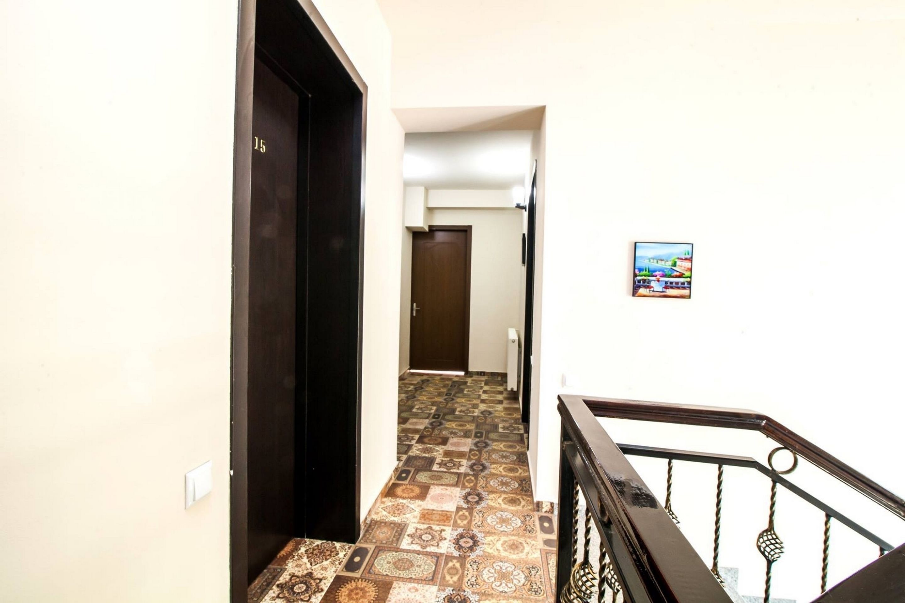 Un pasillo con piso estampado, una puerta oscura y una escalera con barandal de metal.