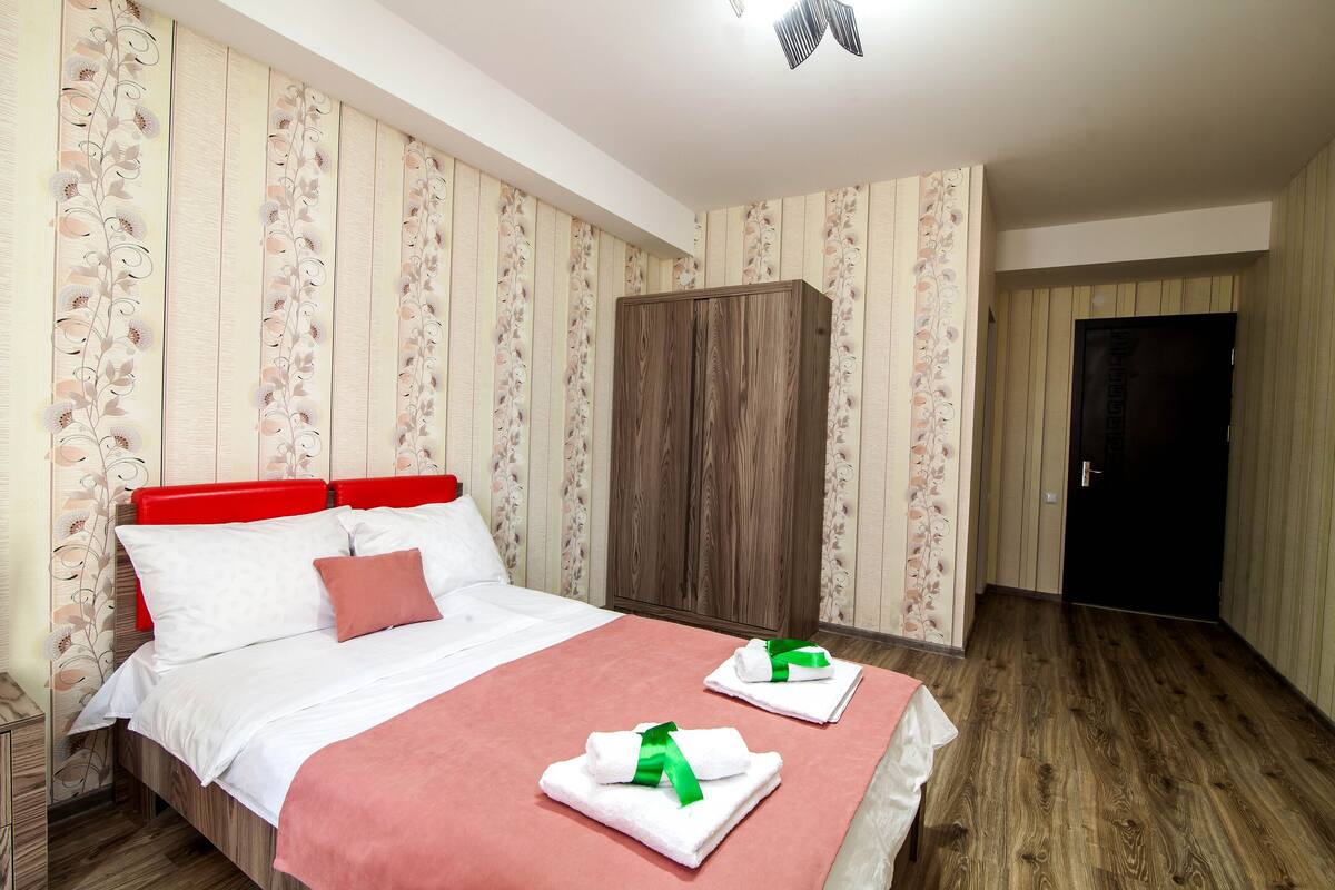 A neatly made bed with white and red bedding, a wooden wardrobe, and a door in the background.
