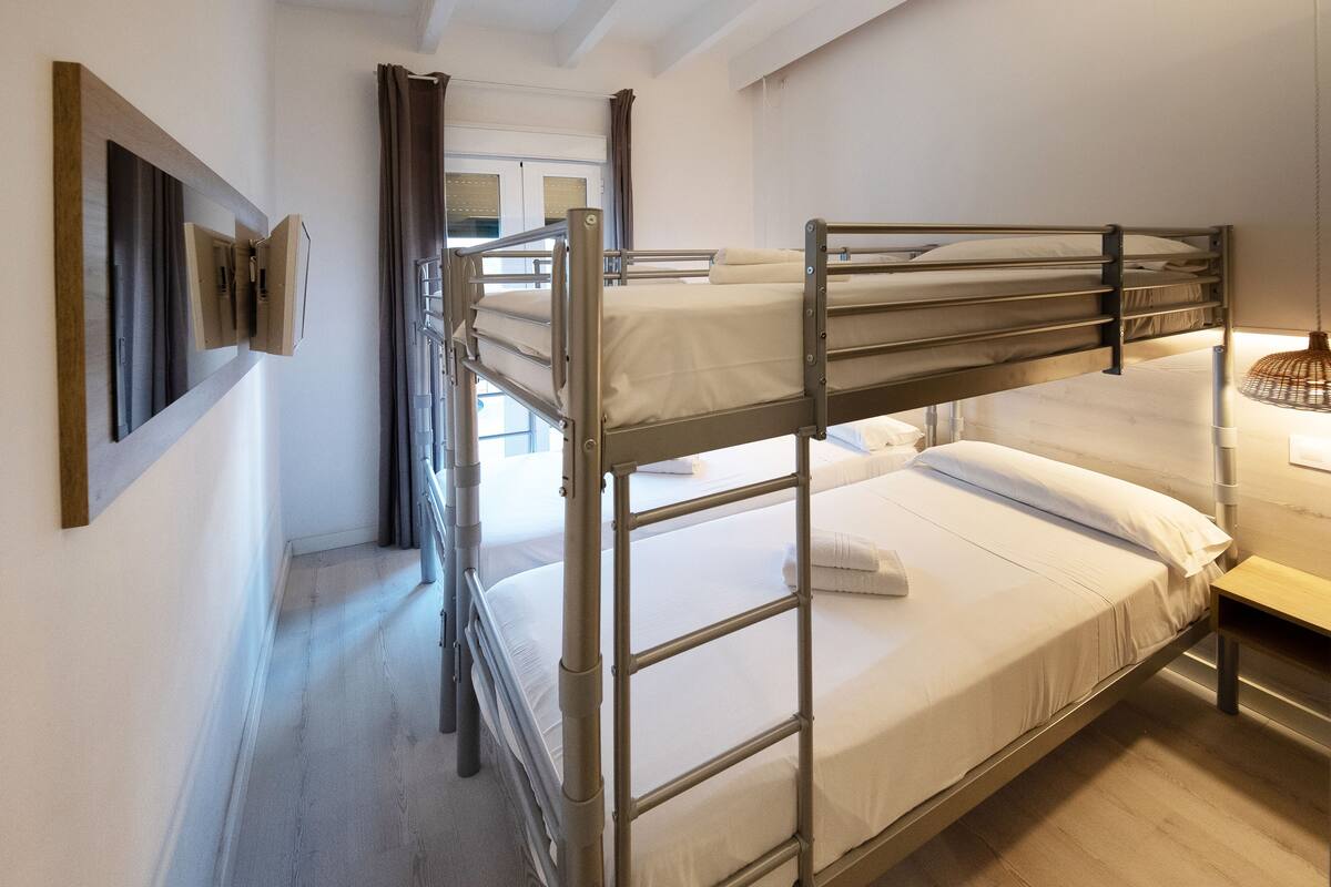 Dormitorio con literas, suelo de madera, una mesita de noche pequeña y una lámpara colgante.