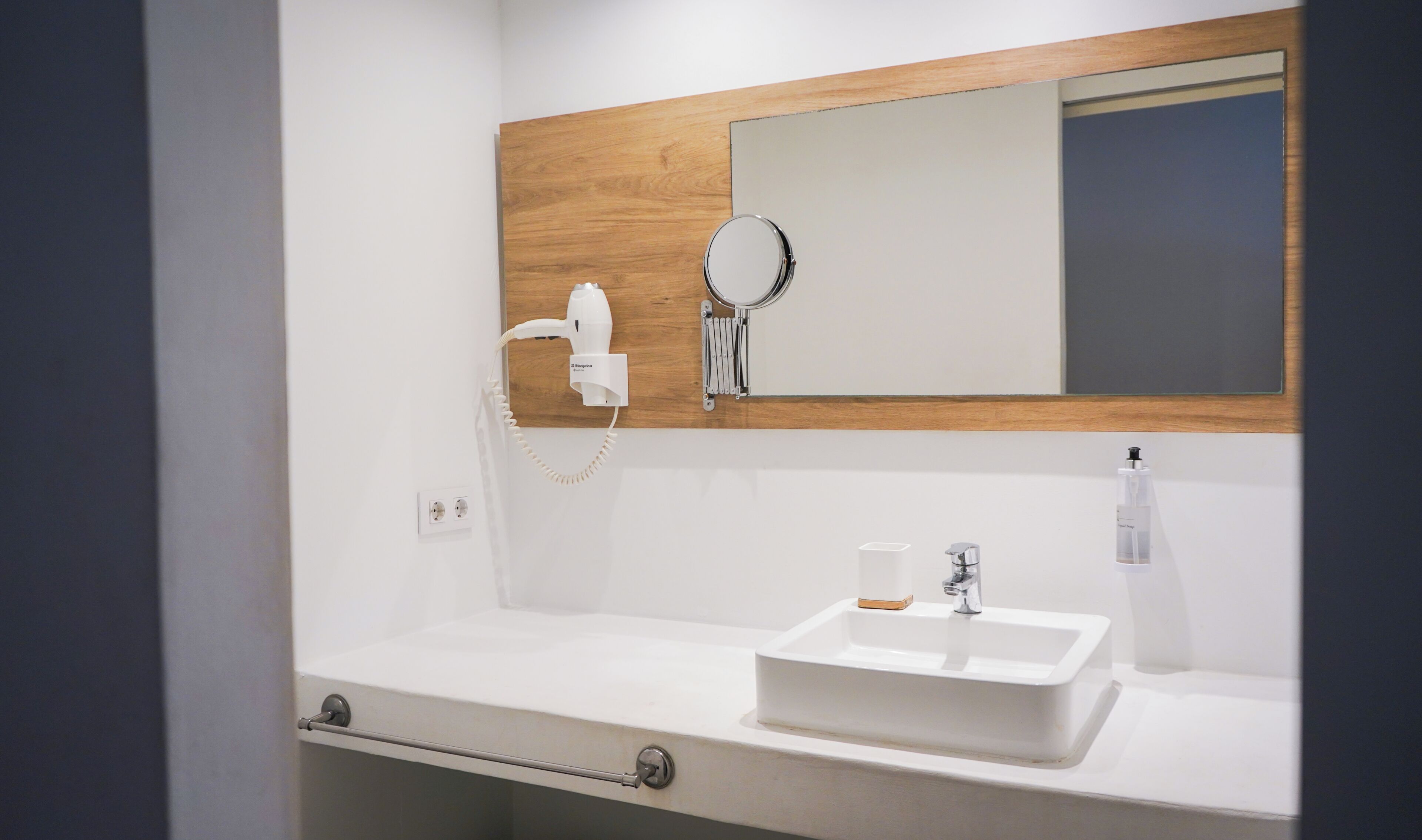 Une salle de bain avec un lavabo blanc, un miroir et un sèche-cheveux fixé au mur.