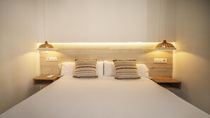 A neatly made bed with two pillows, two bedside tables, and two wall-mounted lamps.