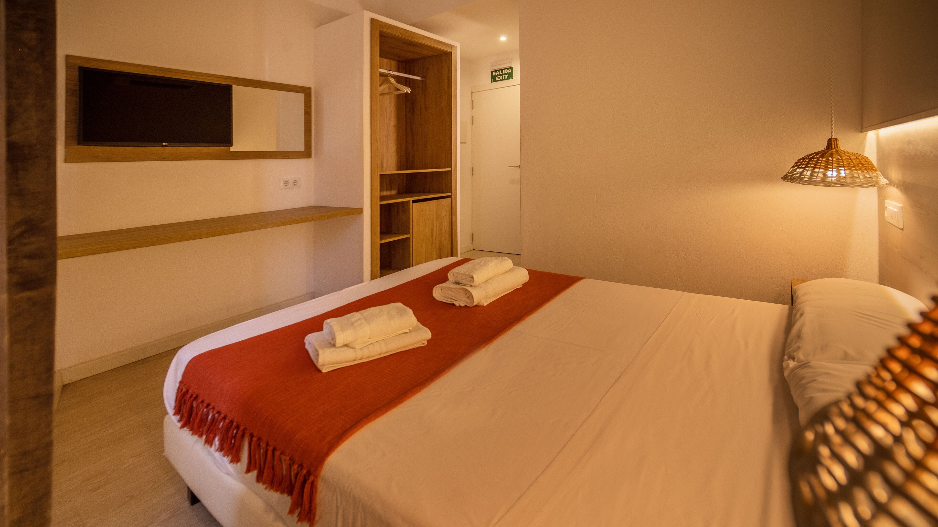 Una habitación de hotel con cama, armario de madera, espejo y lámpara colgante.