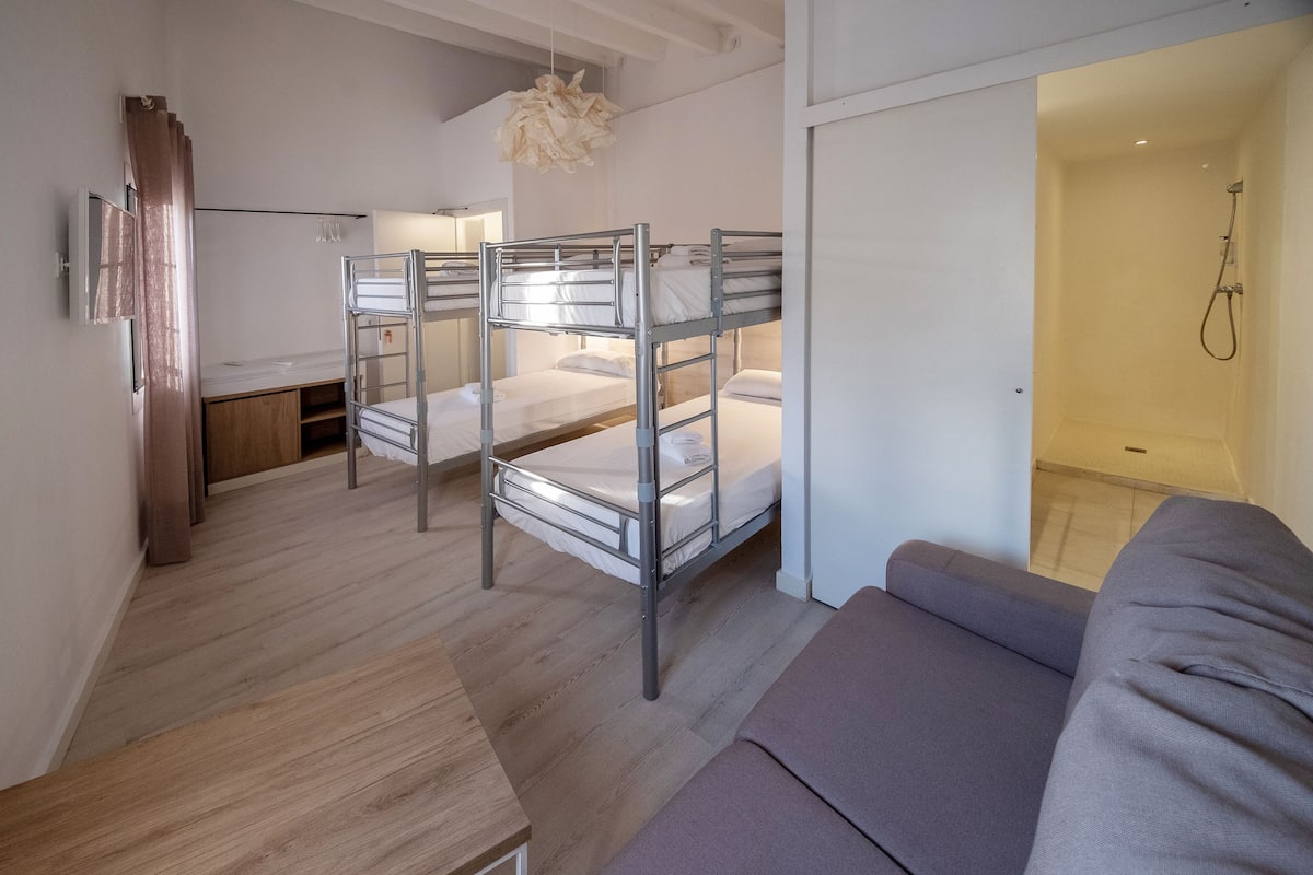 Una habitación moderna y compacta con literas, sofá y zona de ducha.