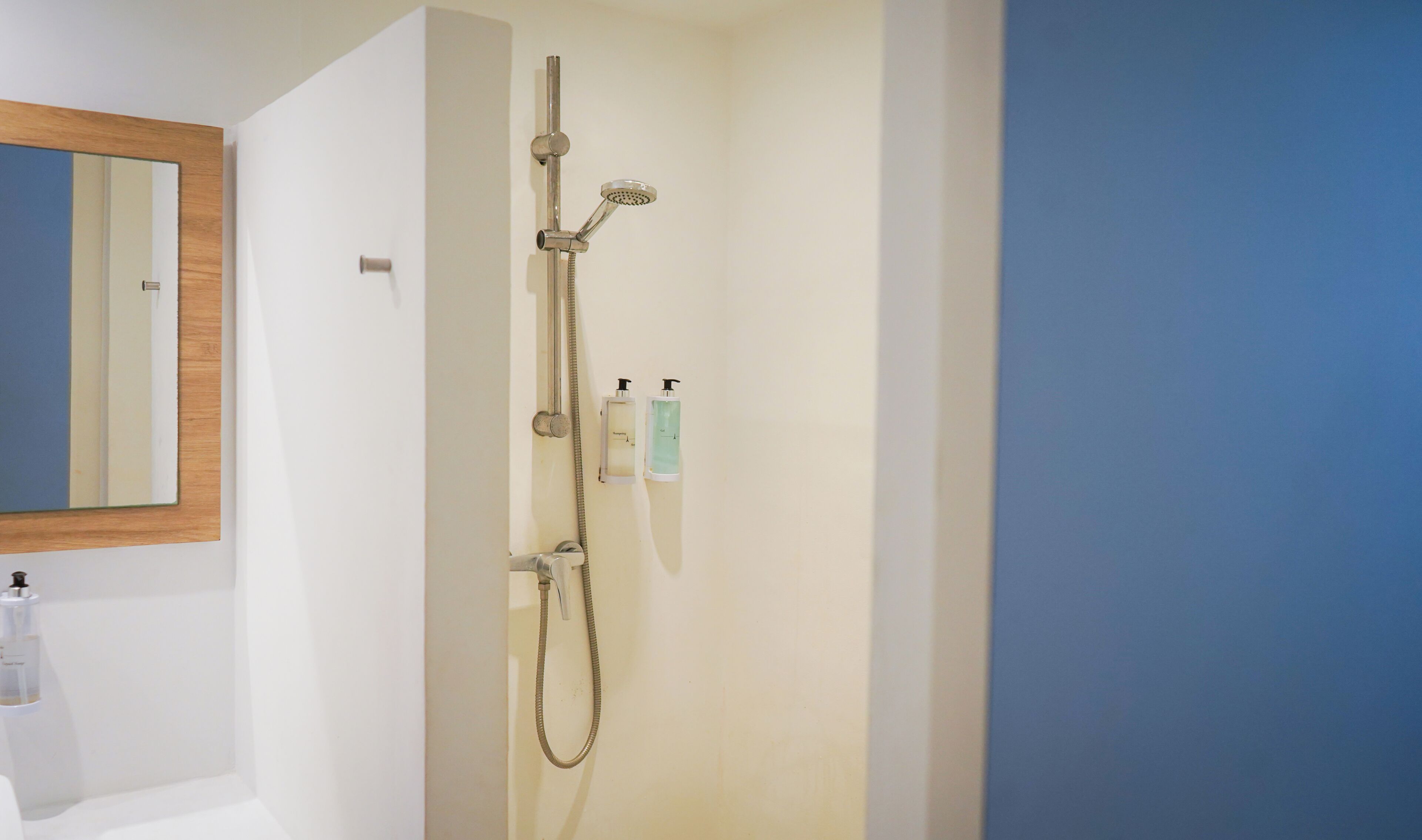 Ducha con cabezal de ducha de mano y grifo empotrado en la pared, un espejo y dos dispensadores de jabón en la pared.