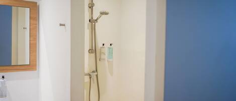 Ducha con cabezal de ducha de mano y grifo empotrado en la pared, un espejo y dos dispensadores de jabón en la pared.