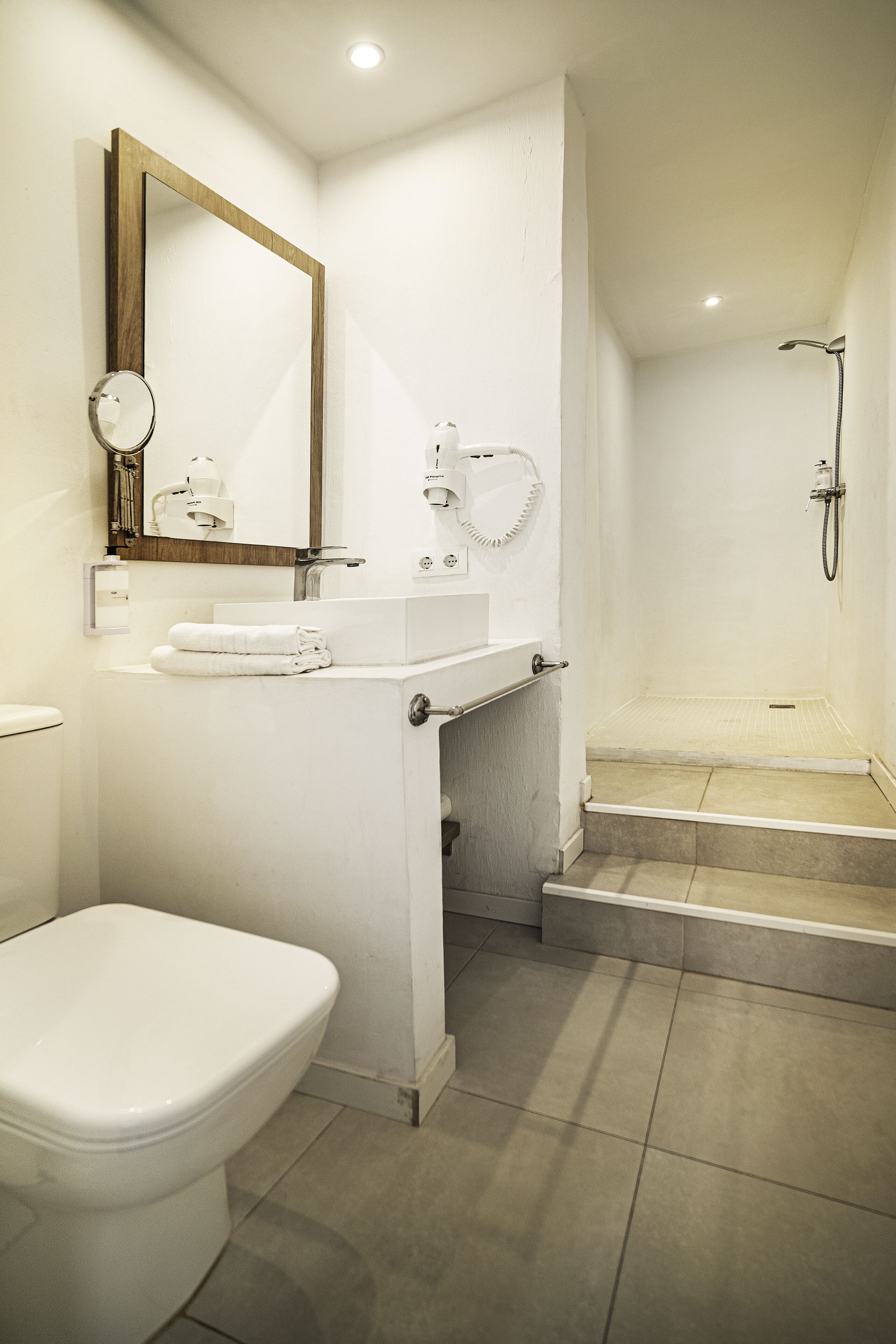 A modern bathroom with a toilet, sink, mirror, and shower.