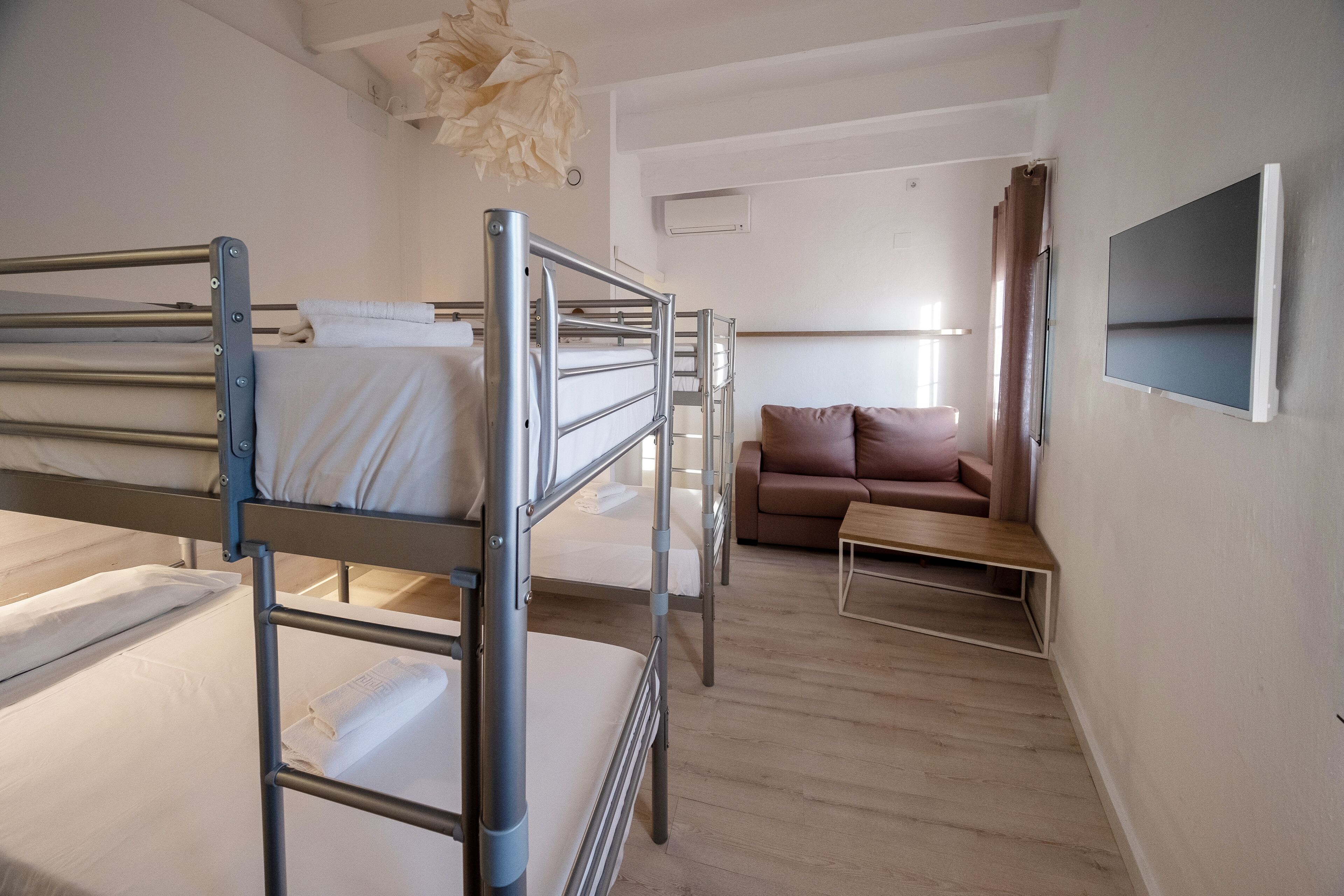 Een hotelkamer met stapelbedden, een slaapbank, een televisie en een houten vloer.