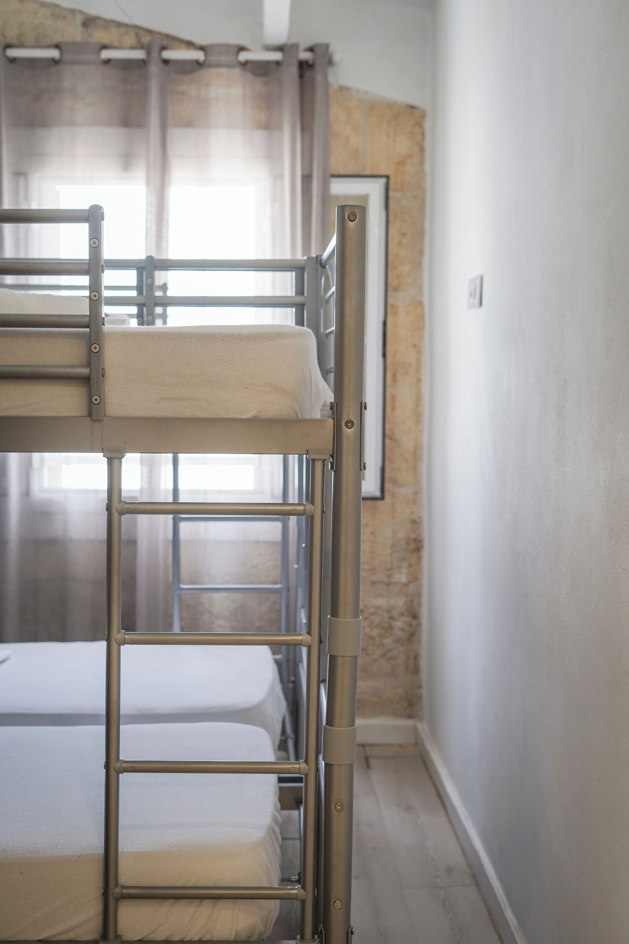 Una cama litera con barandillas metálicas y una ventana con cortinas.