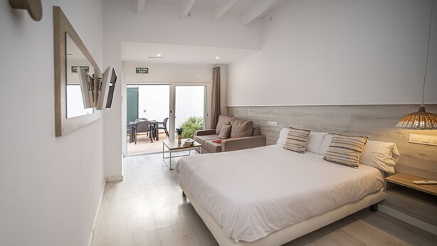 A modern bedroom with a large bed, a sofa, and a dining area in the background.