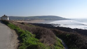 A coastal road with a white house on the left, leading to a beach with waves crashing onto the shore. - Peaceful Rural Location Set Within 5 Acres Of Pasture and Woodland, pet friendly (Great Torrington)