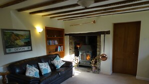 A cozy living room with a black leather sofa, a bookshelf, a stone fireplace, and a wooden door. - Peaceful Rural Location Set Within 5 Acres Of Pasture and Woodland, pet friendly (Great Torrington)