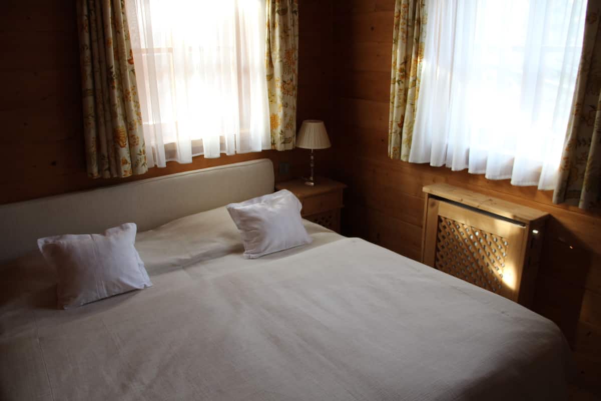 Una cama doble con ropa blanca en una habitación de madera con cortinas florales.
