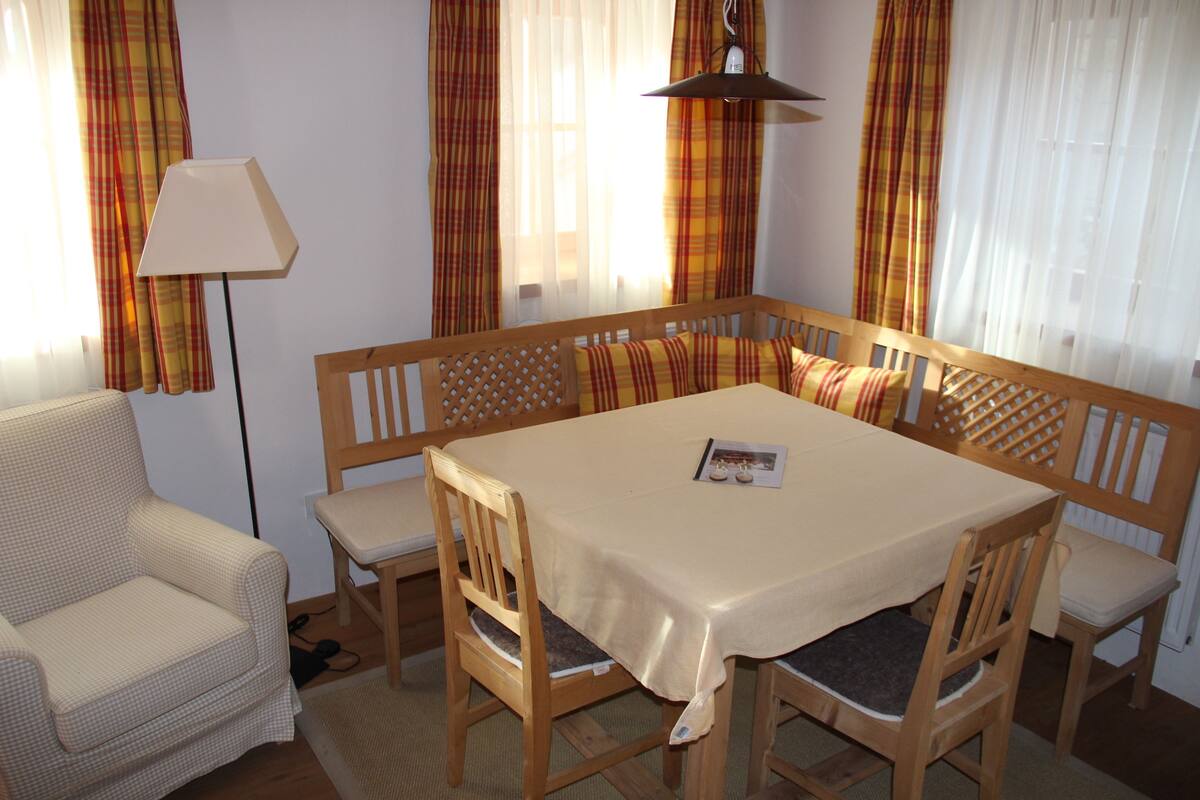 Un comedor con una mesa y sillas de madera, una lámpara y cortinas a cuadros.