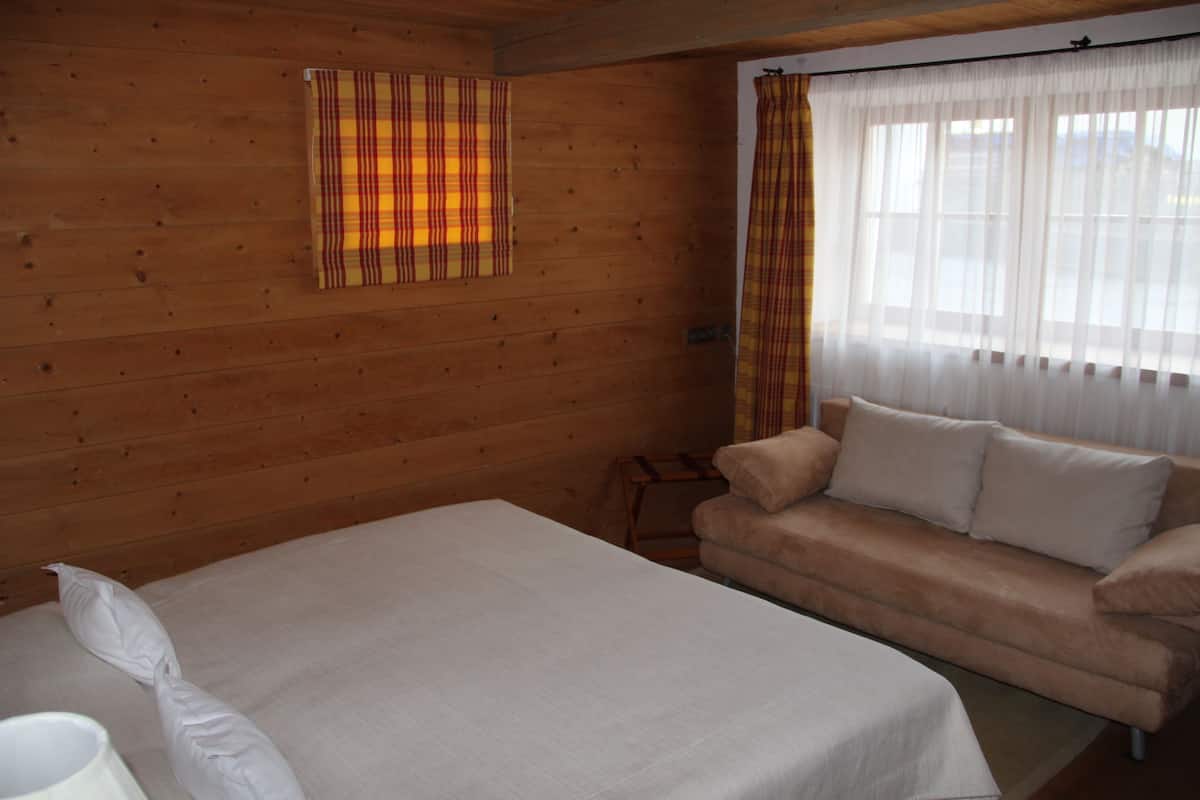 Una habitación con paredes de madera, una cama, un sofá y una ventana con cortinas traslúcidas.