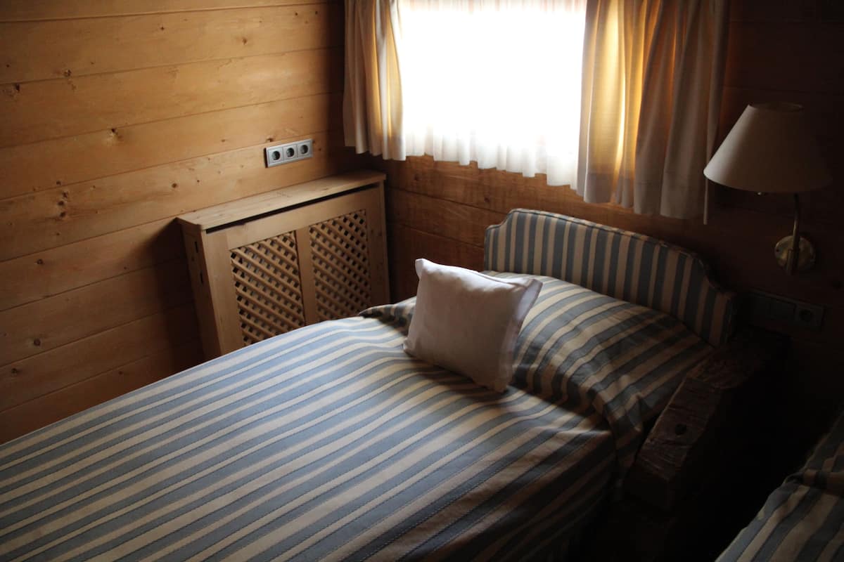 Una cama individual con ropa de cama a rayas en una habitación tipo cabaña con paredes de madera y una ventana con cortinas.